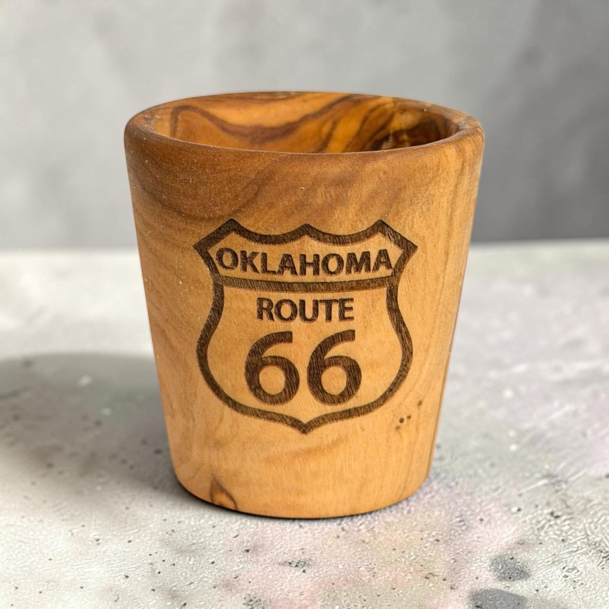 Laser engraved Oklahoma Route 66 olive wood shot glass standing on a tabletop, wooden Route 66 travel souvenir with visible natural wood grain