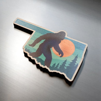 Angled view of Oklahoma Bigfoot Sasquatch wooden magnet showing state outline shape and colorful forest sunset design, novelty Oklahoma magnet
