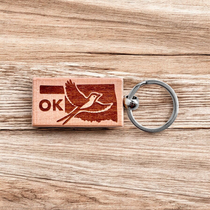 Laser engraved Oklahoma scissor-tailed flycatcher wooden keychain resting on wood surface, Oklahoma bird keychain used as travel souvenir, Route 66 gift, or everyday carry accessory