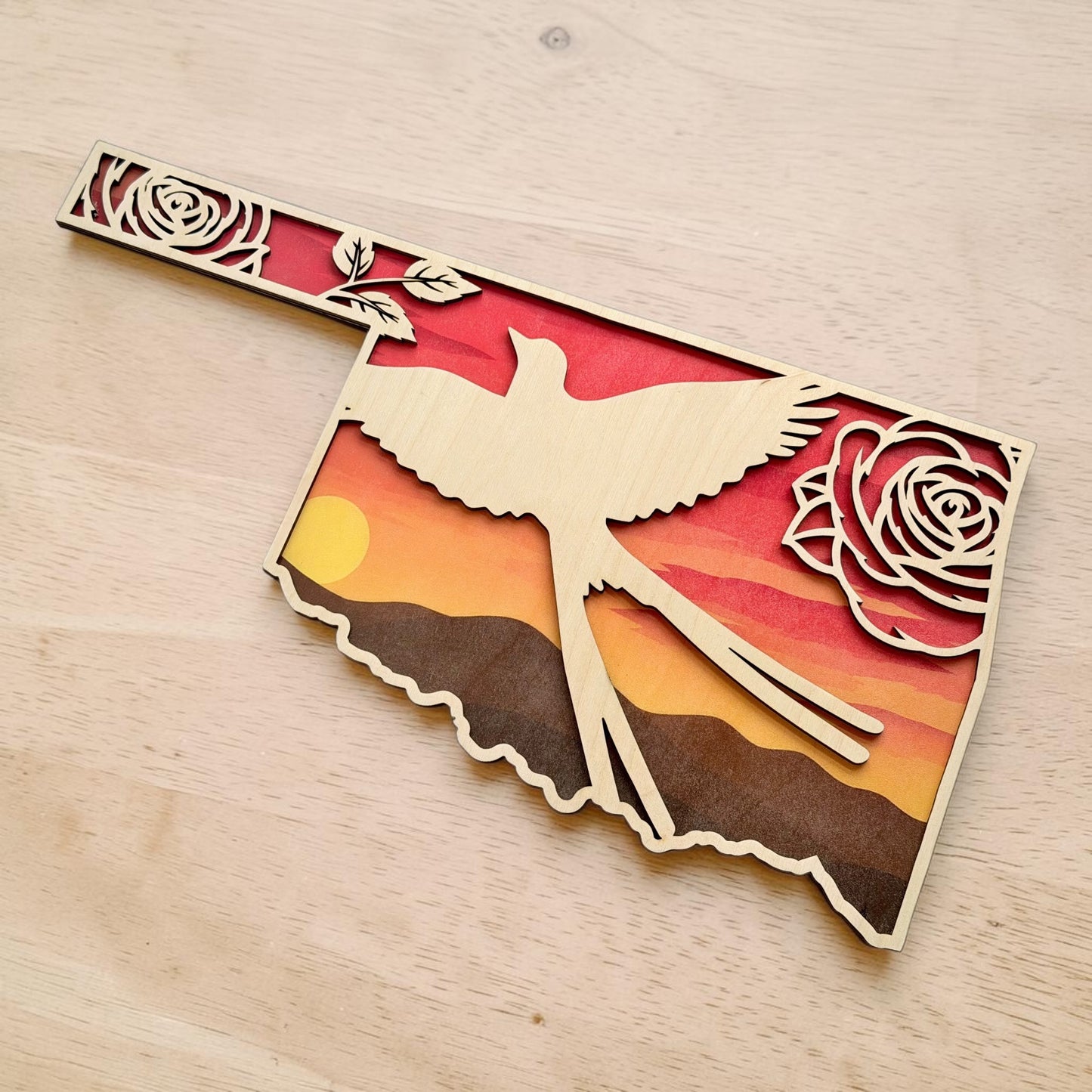 Angled tabletop view of Oklahoma Scissortail Flycatcher sunset wall art with layered wood Oklahoma outline, floral rose details, and western prairie sunset scenery