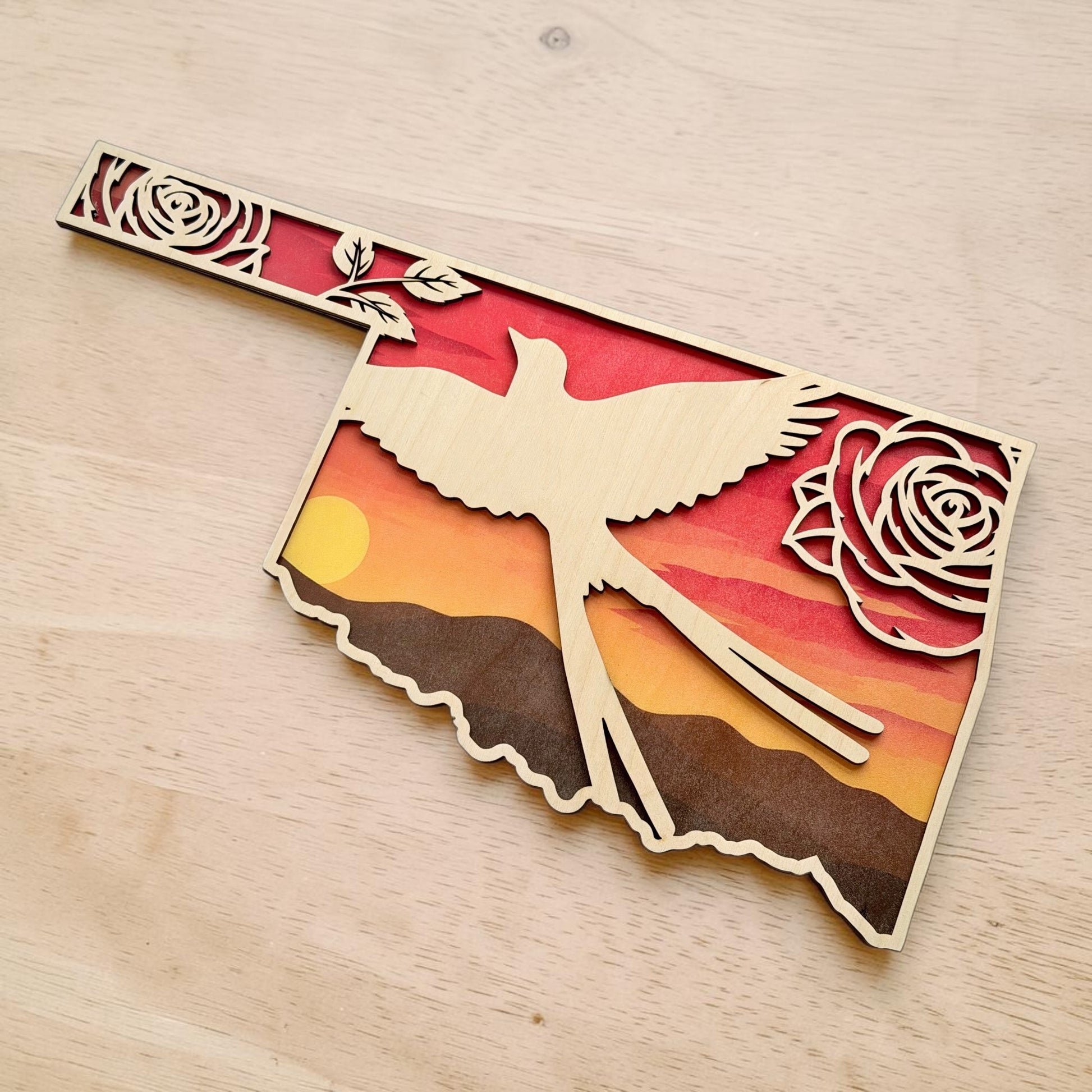 Angled tabletop view of Oklahoma Scissortail Flycatcher sunset wall art with layered wood Oklahoma outline, floral rose details, and western prairie sunset scenery