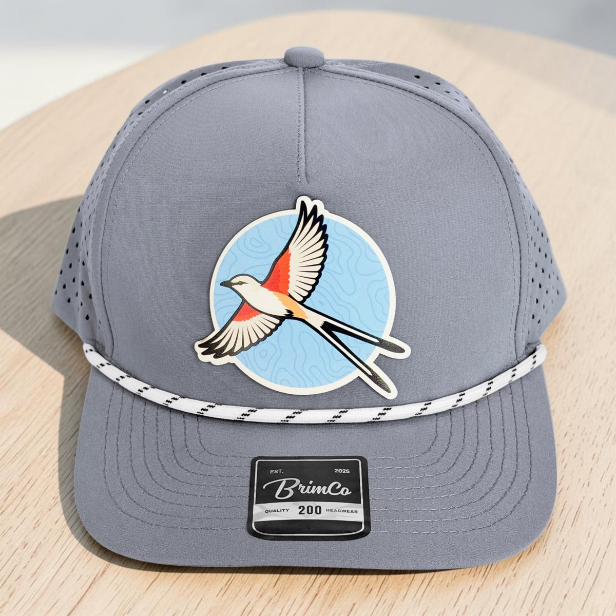Close angled view of gray performance rope hat with Oklahoma scissor-tailed flycatcher patch, laser-perforated panels, structured crown, and stitched precurved bill