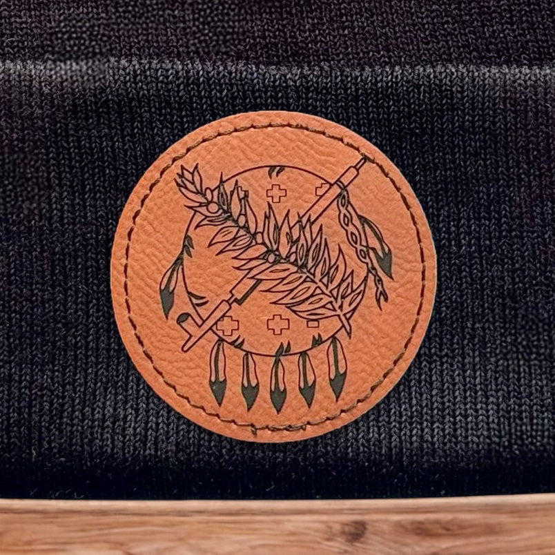 Close up of engraved leatherette patch on black Oklahoma symbol beanie showing feather and arrow artwork and stitched edge