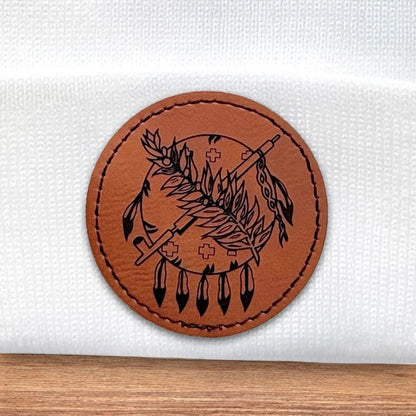 Close up of leatherette patch on white Oklahoma beanie showing engraved feather arrow symbol and stitched border