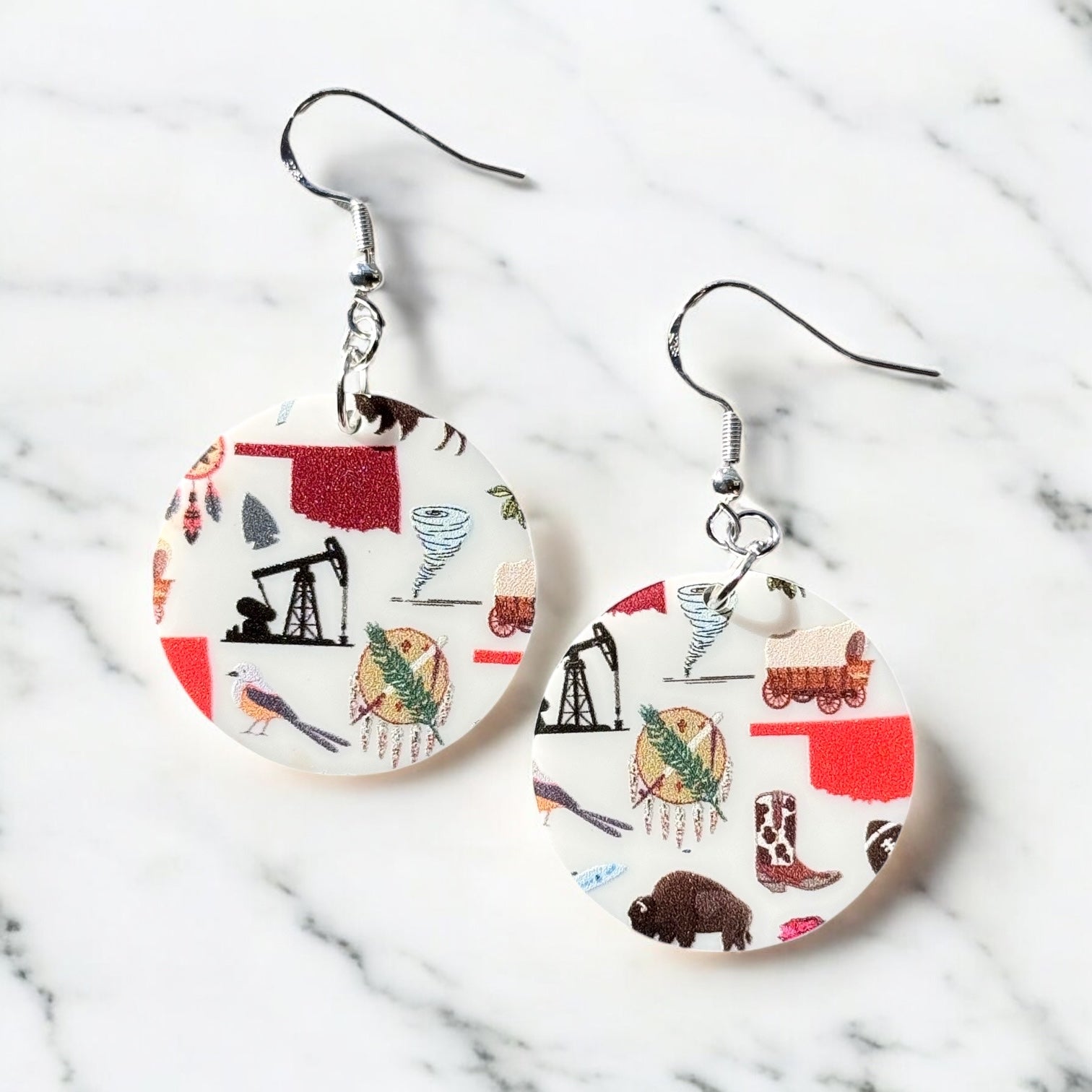 Pair of round acrylic Oklahoma symbol earrings with sterling silver ear hooks displayed on marble surface