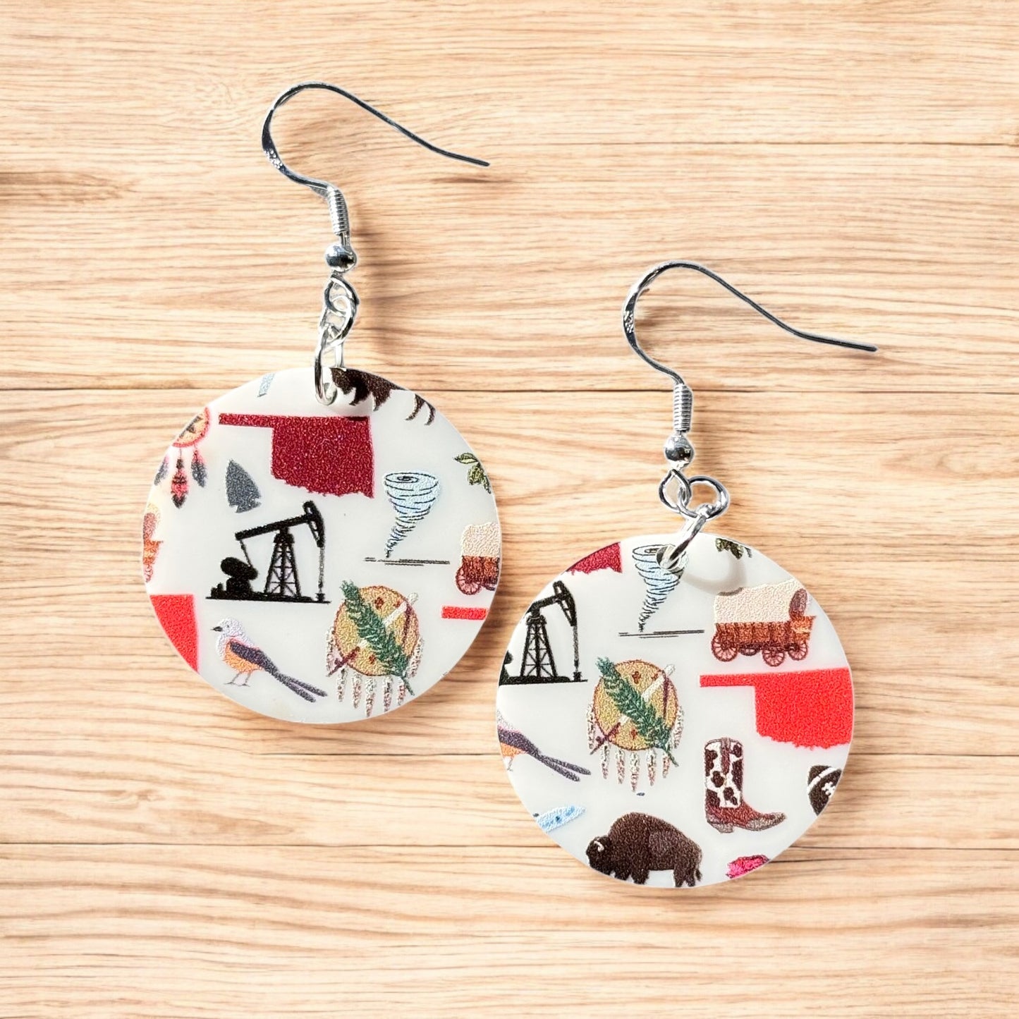 Pair of round acrylic Oklahoma symbol earrings with sterling silver ear hooks displayed on wood surface