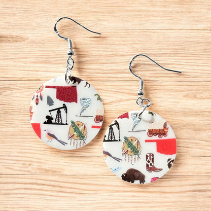 Pair of round acrylic Oklahoma symbol earrings with sterling silver ear hooks displayed on wood surface