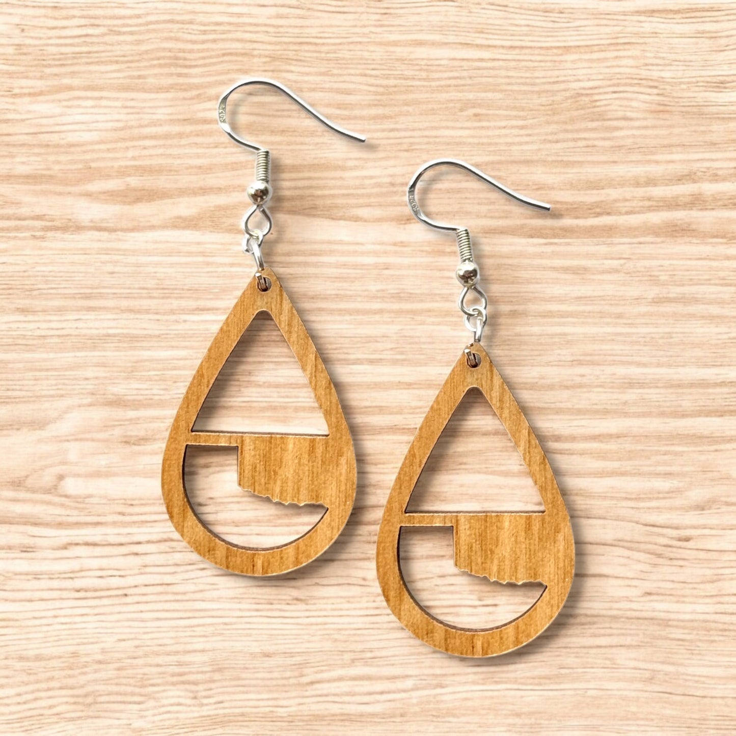 Flat lay of Oklahoma wooden teardrop earrings showing natural wood grain and Oklahoma state silhouette cutout, lightweight state pride jewelry