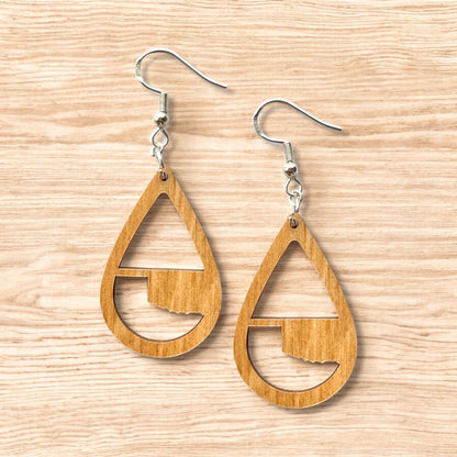 Flat lay of Oklahoma wooden teardrop earrings showing natural wood grain and Oklahoma state silhouette cutout, lightweight state pride jewelry