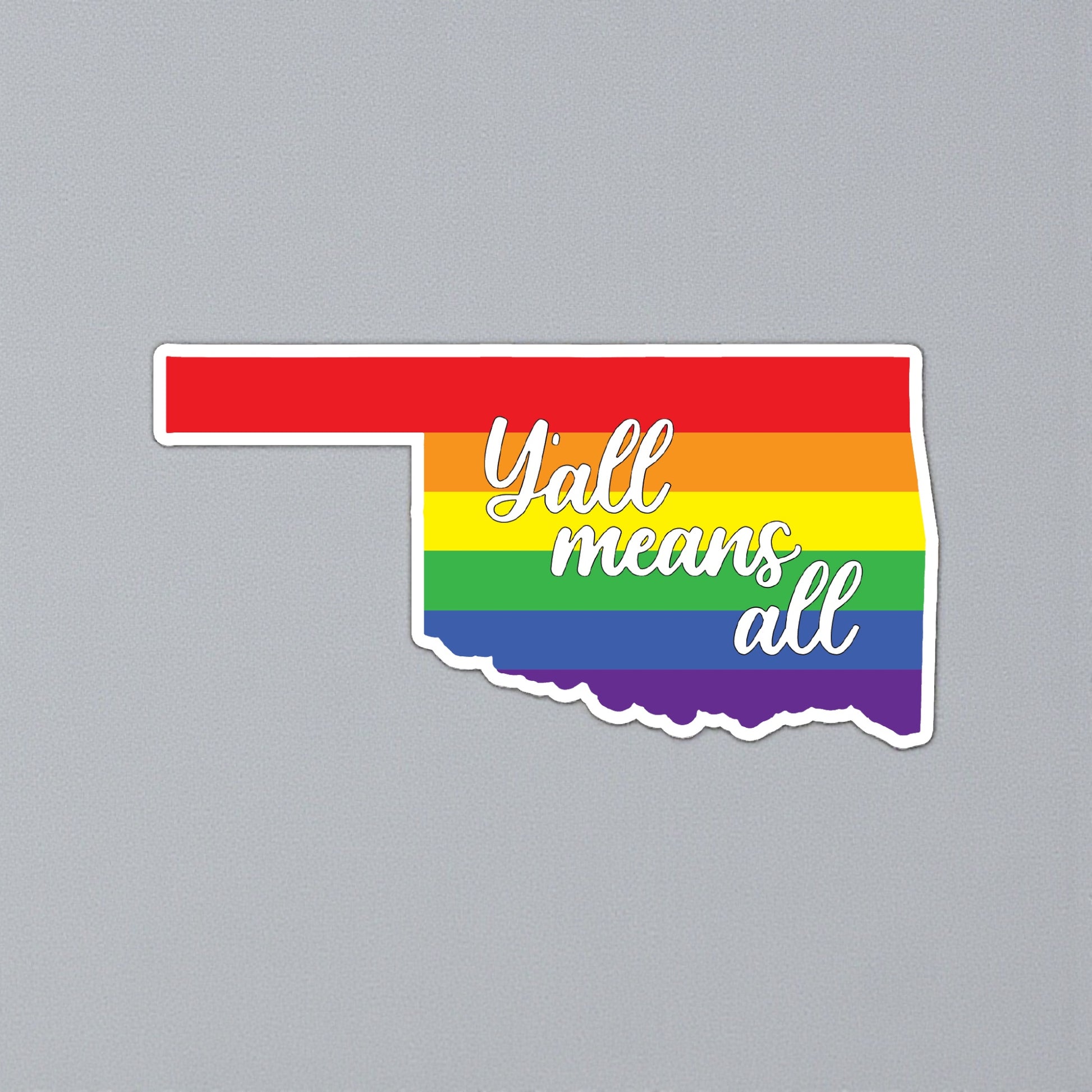 Oklahoma state outline pride sticker displayed on gray background, Yall Means All rainbow vinyl decal for Tulsa and Oklahoma gift shops