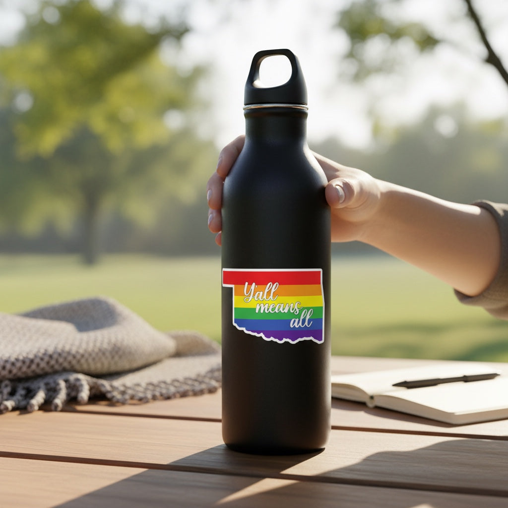 Oklahoma Yall Means All pride vinyl sticker applied to black metal water bottle outdoors, rainbow Oklahoma state decal supporting inclusion and community