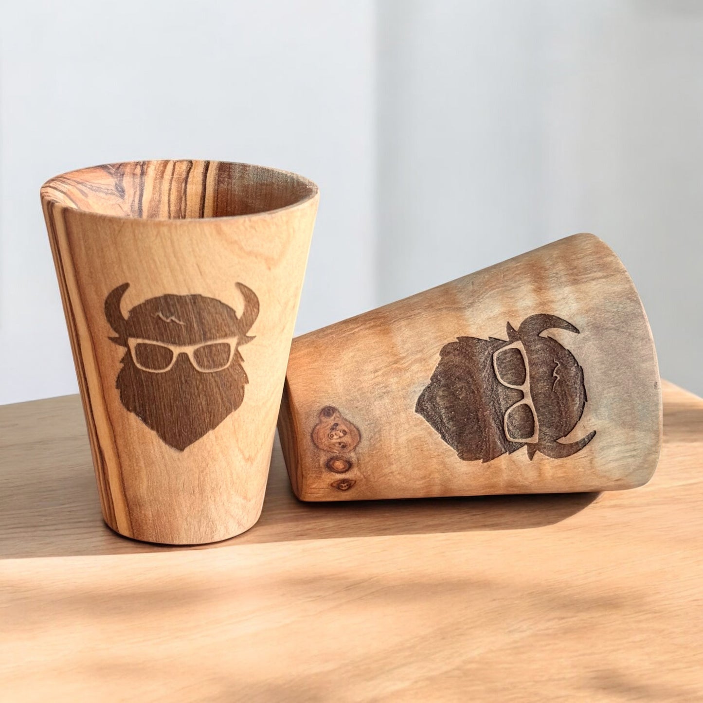 Two olive wood shot glasses showing engraved bison logo and natural grain, handcrafted wood shot glasses for home bar or gift