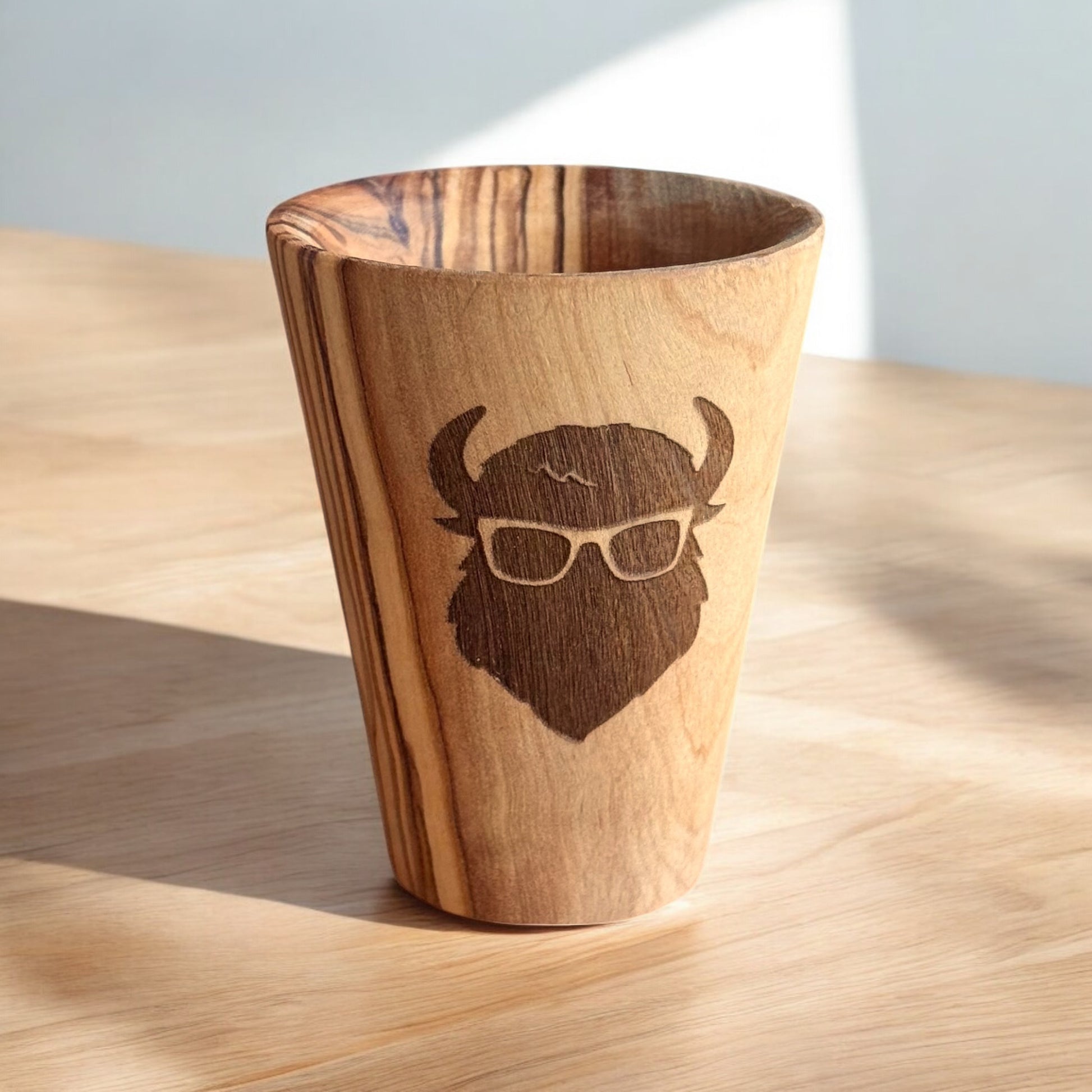 Single olive wood shot glass with laser engraved bison design sitting on wood surface, rustic barware gift