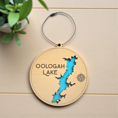 Flat lay of Oologah Lake layered wooden ornament showing engraved lake name, compass detail, and blue painted water layer beneath laser cut wood top