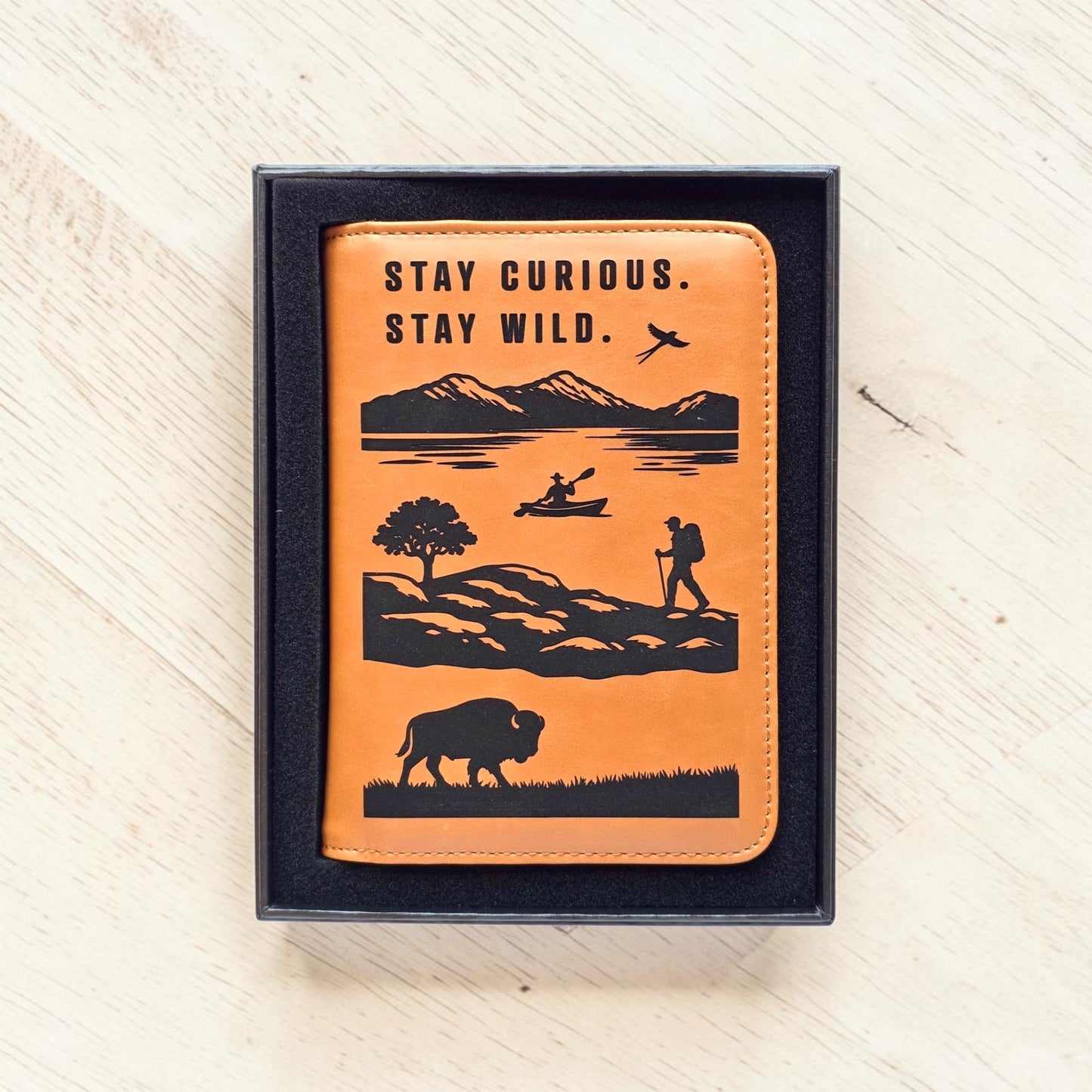 Adventure passport wallet displayed inside black gift box with engraved travel scene and Stay Curious Stay Wild message, ready to gift passport cover for travel lovers