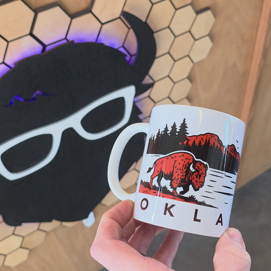Video showing off the 11oz coffee mug rotating around. Oklahoma wildlife coffee mug featuring canoe paddler on lake at sunrise with mountain silhouette and forest landscape, Oklahoma souvenir mug with outdoor adventure theme