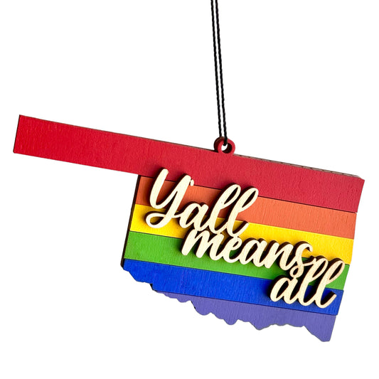 Pride-themed Oklahoma ornament featuring rainbow layers and a laser-cut “Y’all Means All” message, hanging on a black string