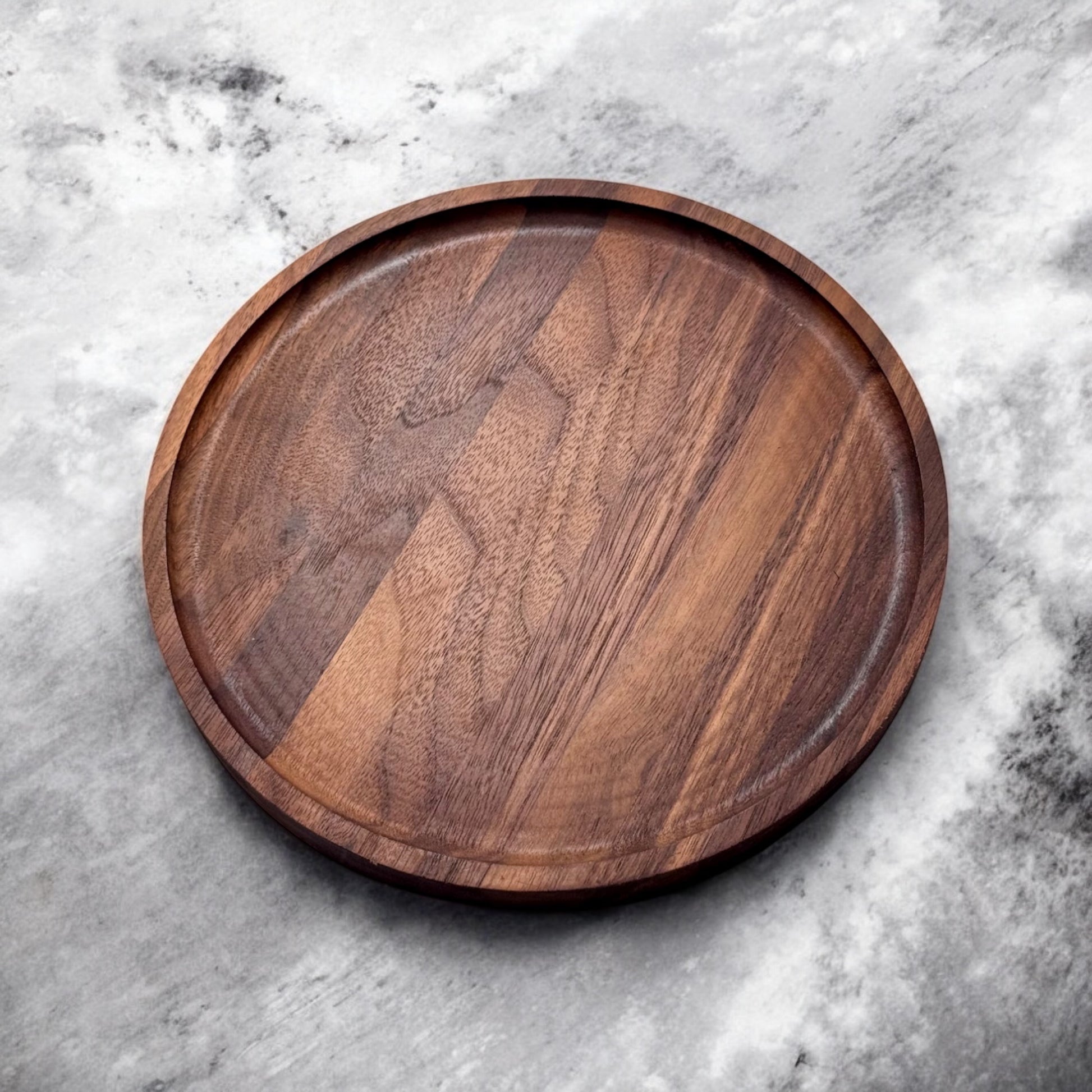 Angled photo of a round solid walnut charcuterie board with a smooth finish on marble background