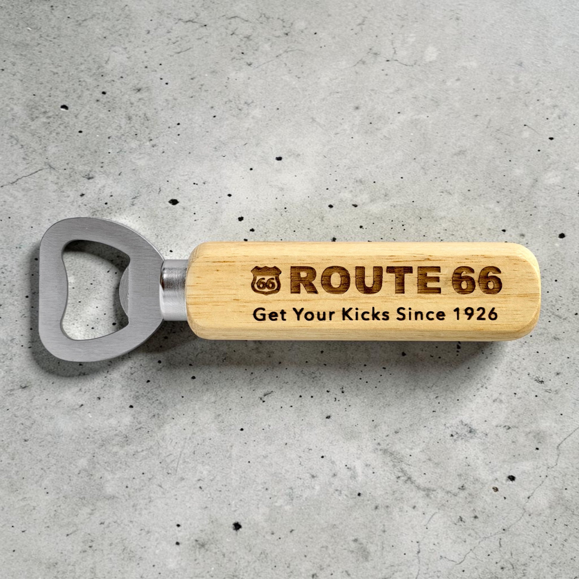 Engraved Route 66 wooden bottle opener displayed on gray concrete surface showing retro highway souvenir design and stainless steel bottle opener head