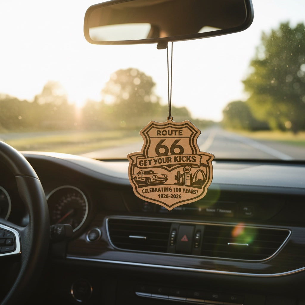 Route 66 Centennial wood ornament hanging from rearview mirror inside car at sunset, engraved Route 66 souvenir for road trip travelers and highway keepsake collectors
