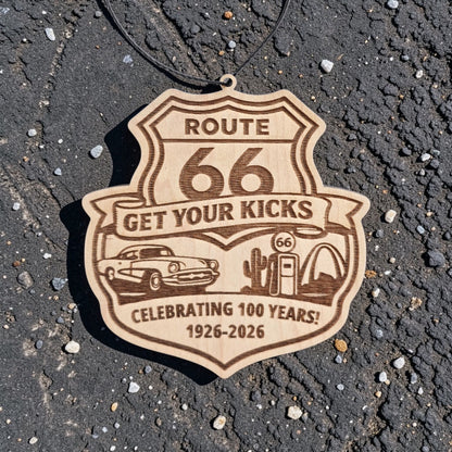 Route 66 Centennial wood ornament placed on asphalt road surface, engraved highway shield souvenir celebrating 1926 to 2026 travel history
