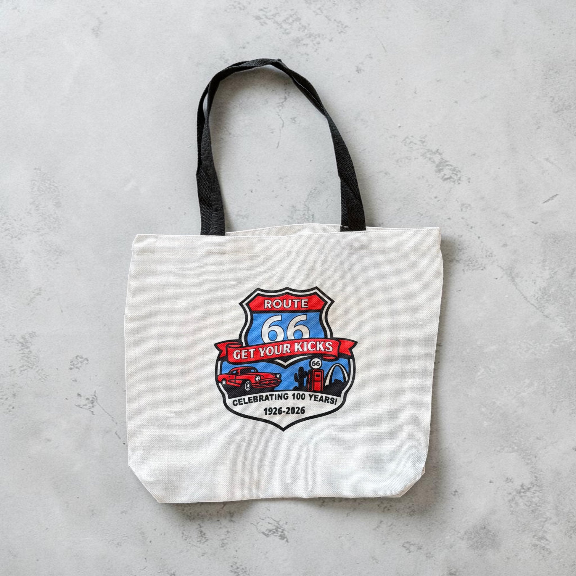 Flat lay view of Route 66 commemorative tote bag with vintage inspired Route 66 shield artwork, retro car, gas pump, and Americana travel icons on a white canvas style souvenir tote