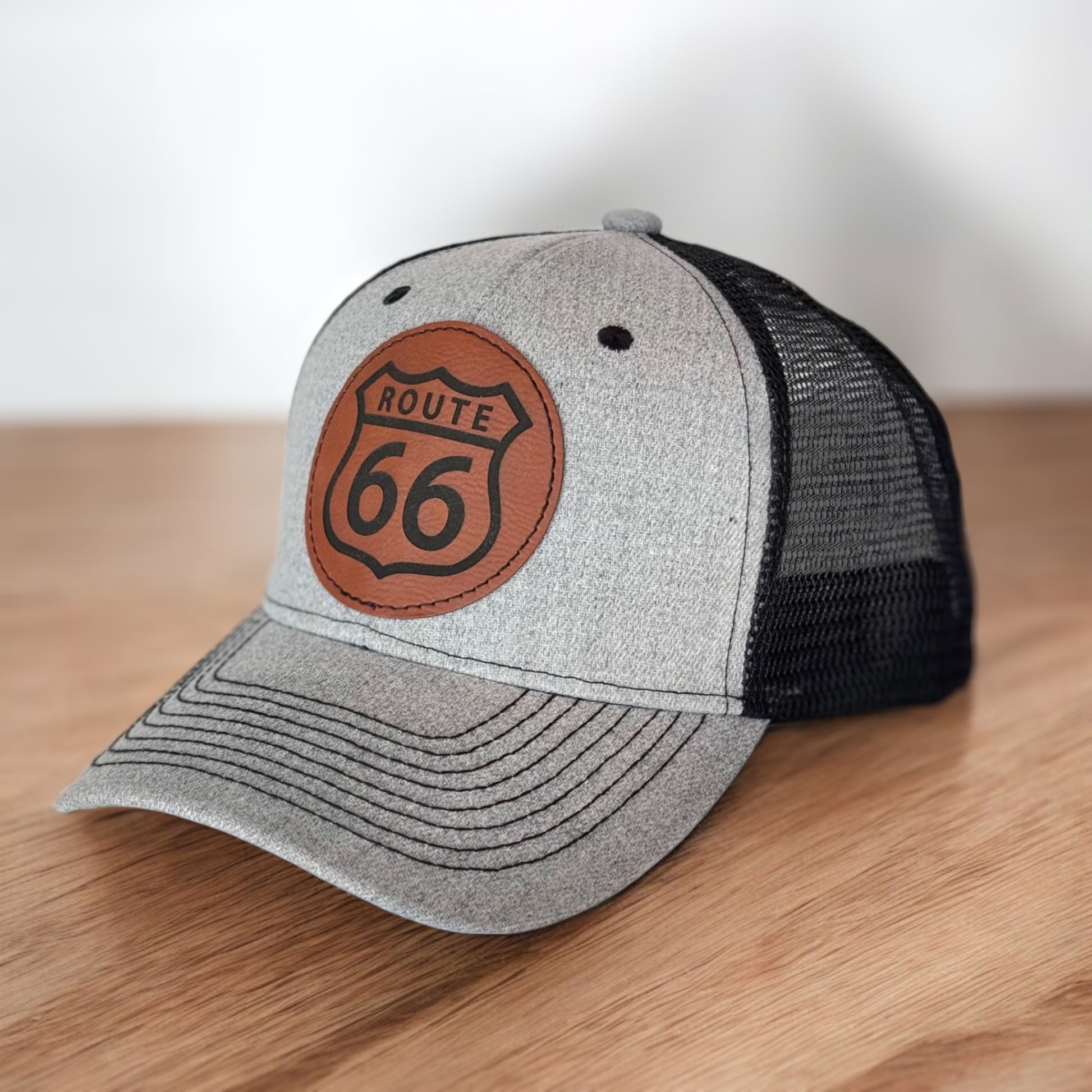 Angled view of gray Route 66 leather patch trucker hat showing curved bill and heat pressed Route 66 shield patch