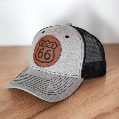 Angled view of gray Route 66 leather patch trucker hat showing curved bill and heat pressed Route 66 shield patch
