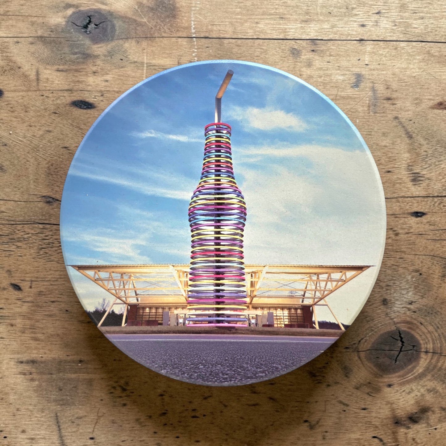 Flat lay of round ceramic Route 66 Pops coaster featuring Oklahoma roadside soda bottle attraction, colorful souvenir drink coaster