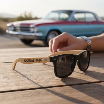 Black Route 66 sunglasses with bamboo arms engraved Route 66 1926 resting on table beside vintage car, stylish road trip sunglasses for travel lovers and souvenir buyers