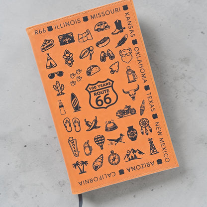 angled view of Route 66 travel icons leatherette notebook showing engraved road trip symbols including cactus, motel sign, motorcycle and Route 66 shield