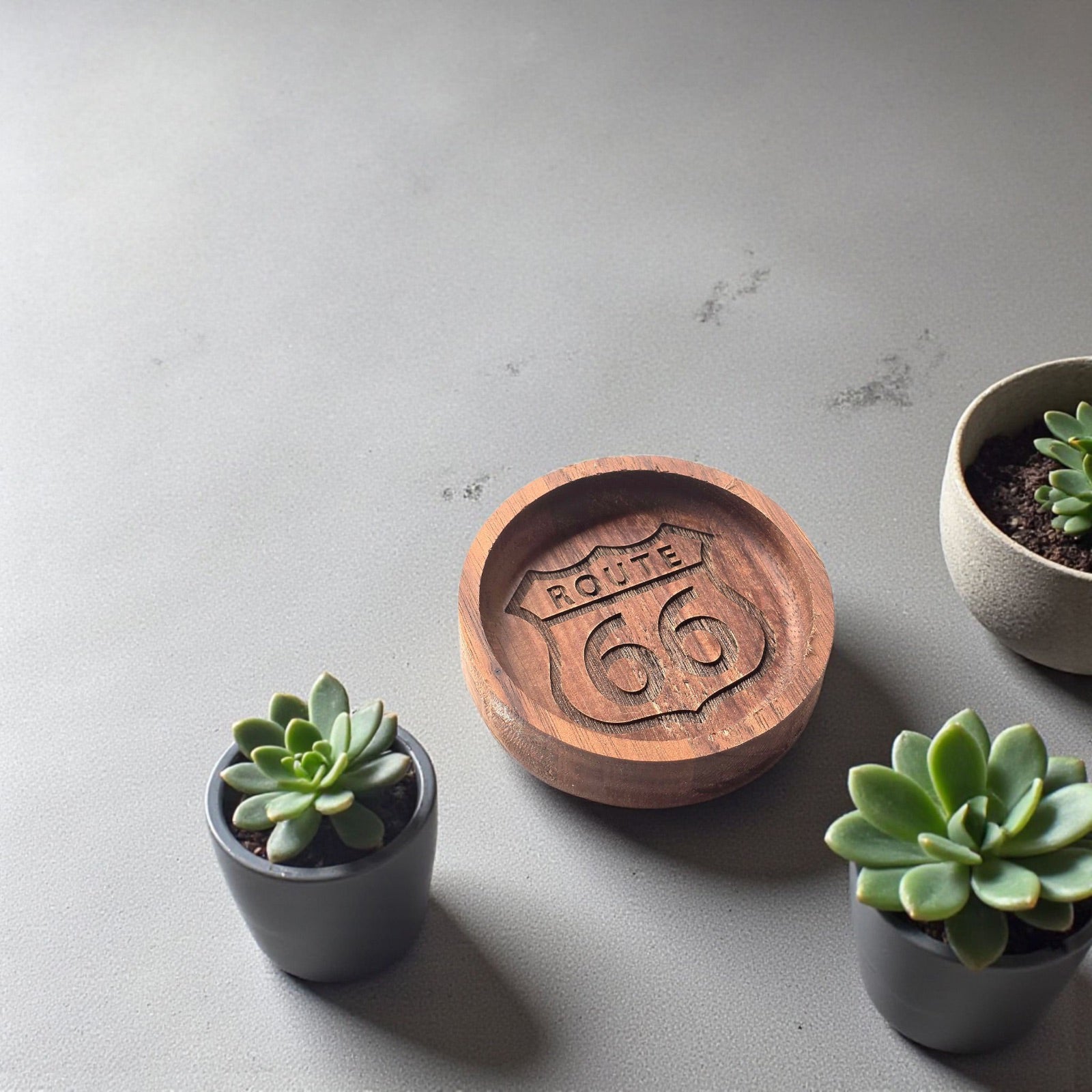 Route 66 walnut ring tray styled on a tabletop with small plants, engraved wooden dish used as a travel themed ring holder or souvenir