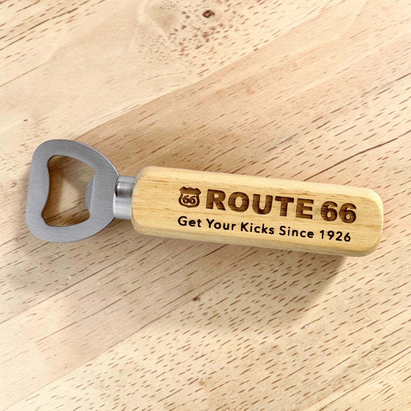 Closeup angled view of Route 66 engraved wooden bottle opener resting on wood tabletop, nostalgic roadside travel gift inspired by historic Route 66