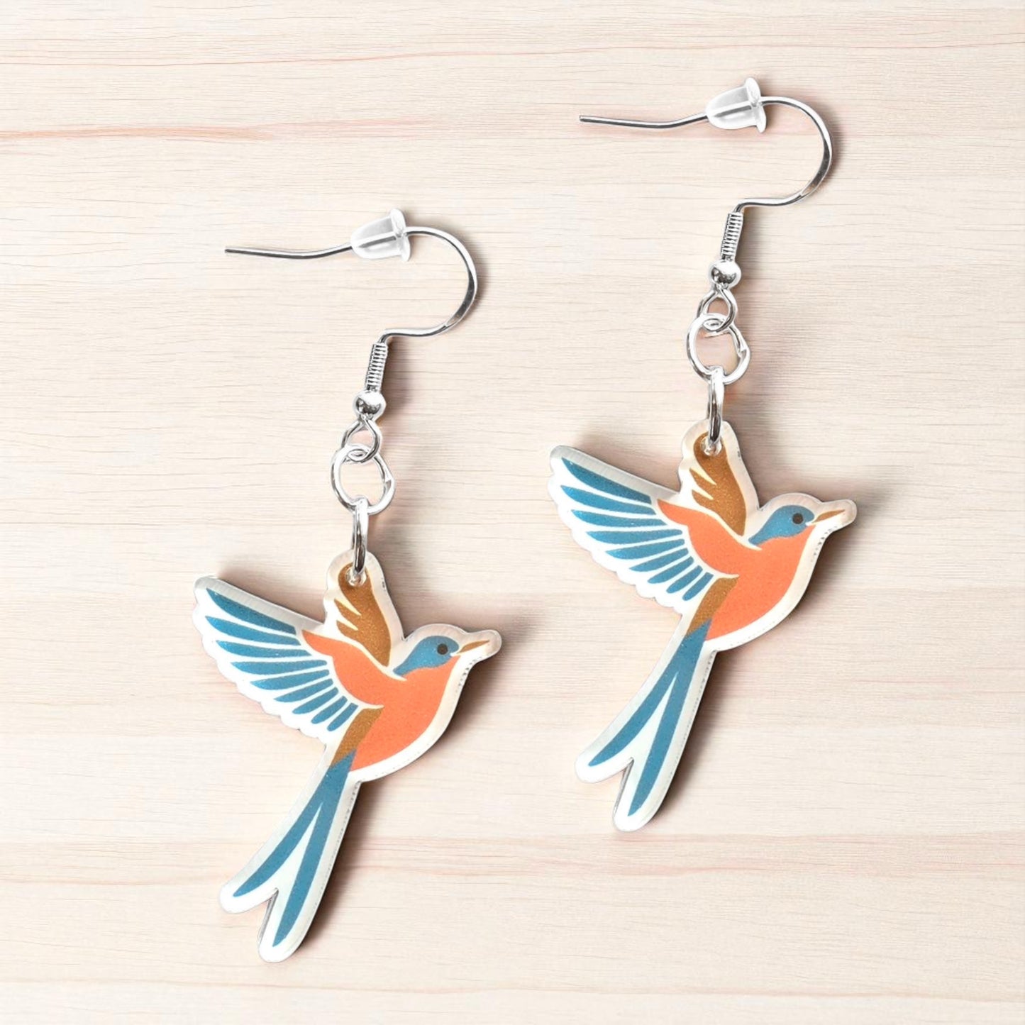 Pair of color scissor-tailed flycatcher acrylic earrings displayed on wood surface, Oklahoma state bird earrings with long tail design for travel souvenir or gift