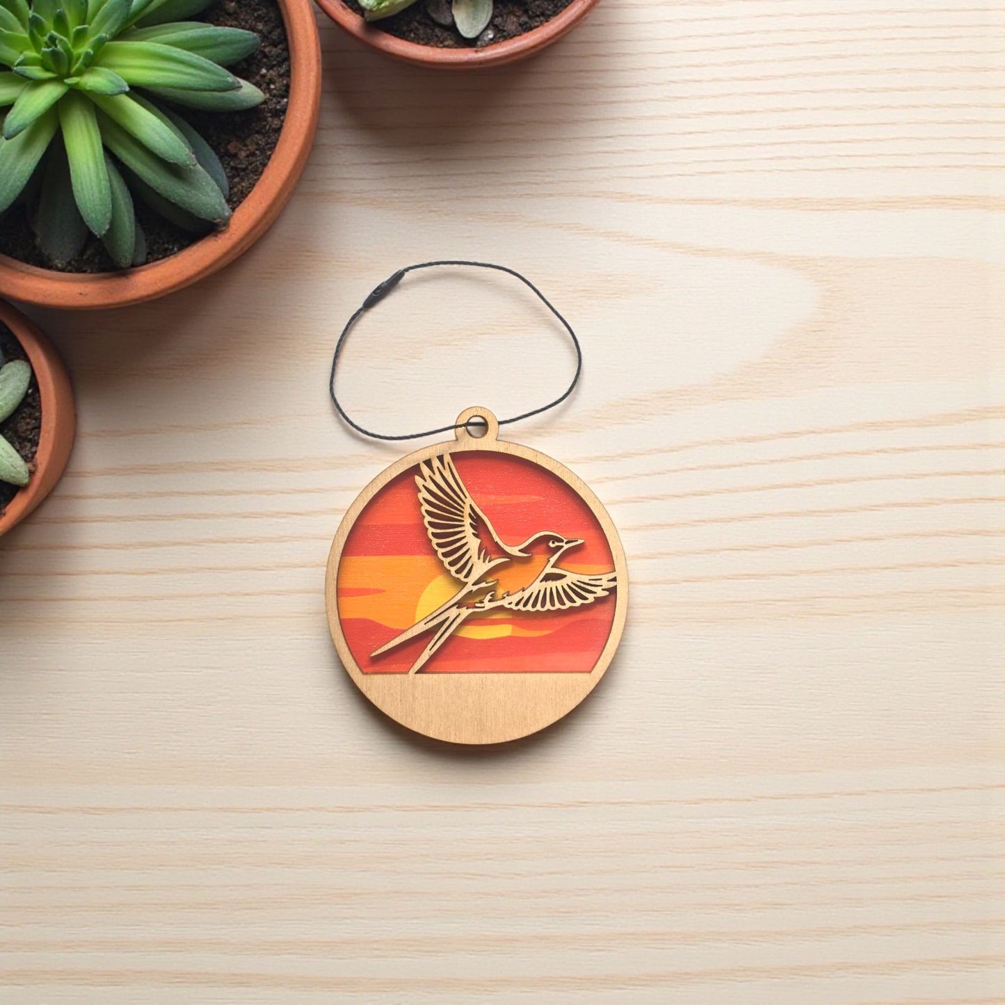 Flat lay of Oklahoma scissor-tailed flycatcher wooden ornament on light wood surface, layered wood ornament showing bird in flight with sunset colors for Oklahoma gift or travel souvenir