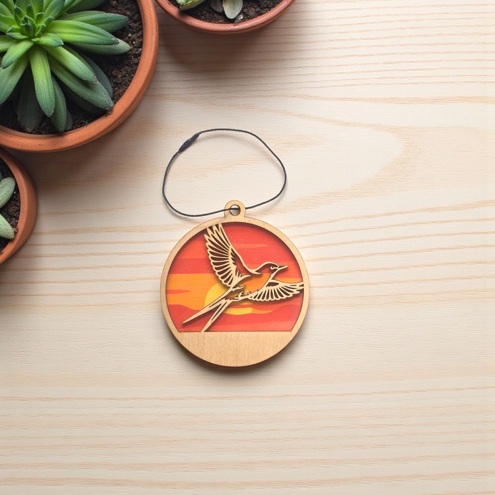 Flat lay of Oklahoma scissor-tailed flycatcher wooden ornament on light wood surface, layered wood ornament showing bird in flight with sunset colors for Oklahoma gift or travel souvenir