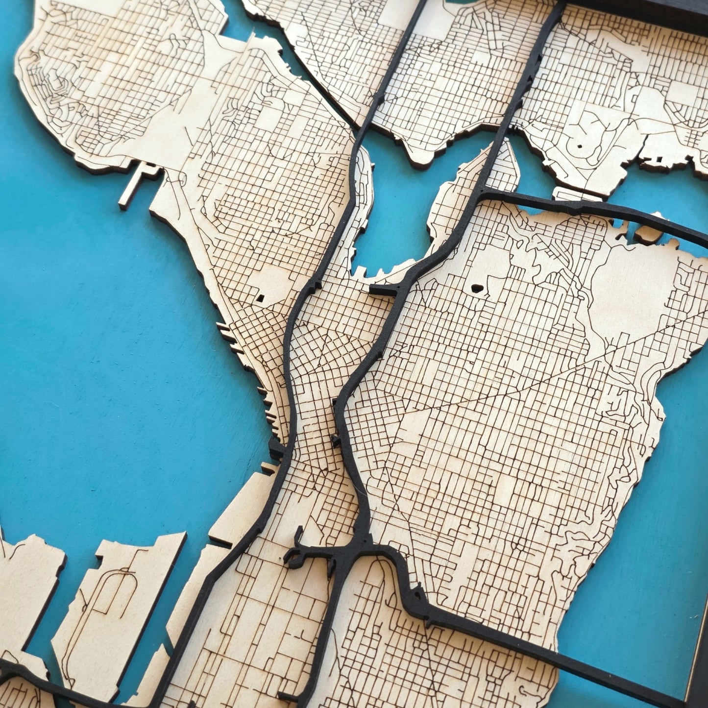 close up of Seattle wooden city map showing engraved street grid and raised road layers, detailed laser cut wood map design with blue background