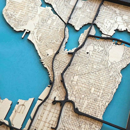 close up of Seattle wooden city map showing engraved street grid and raised road layers, detailed laser cut wood map design with blue background