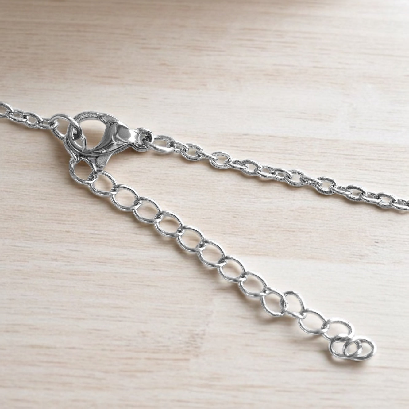 Silver necklace chain extender with lobster clasp and adjustable links on pale wooden surface