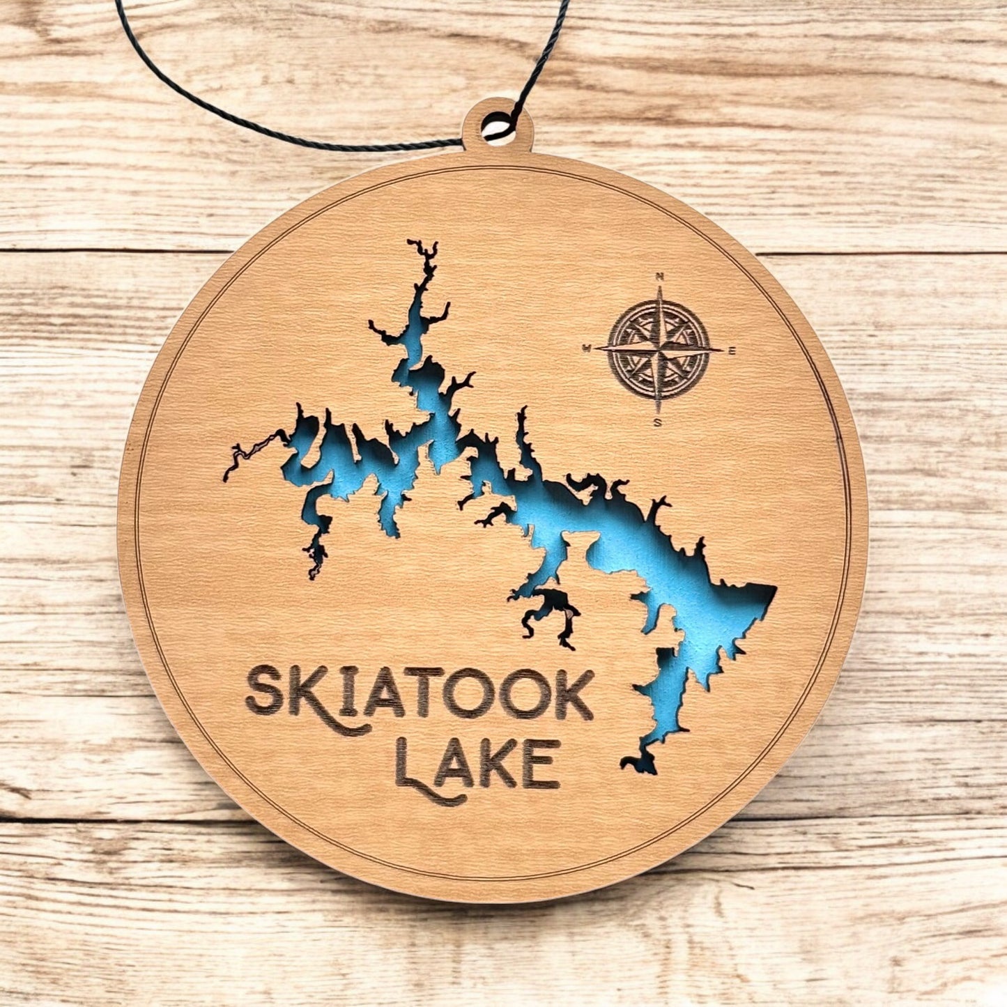 Skiatook Lake layered wood ornament displayed on wood surface, round lake map ornament with engraved text and blue water layer