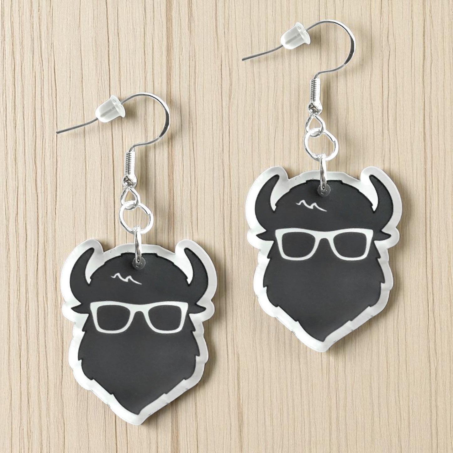 Pair of black and white the curious bison head acrylic earrings displayed on wood surface, graphic bison earrings with sterling silver hooks for travel or souvenir gift