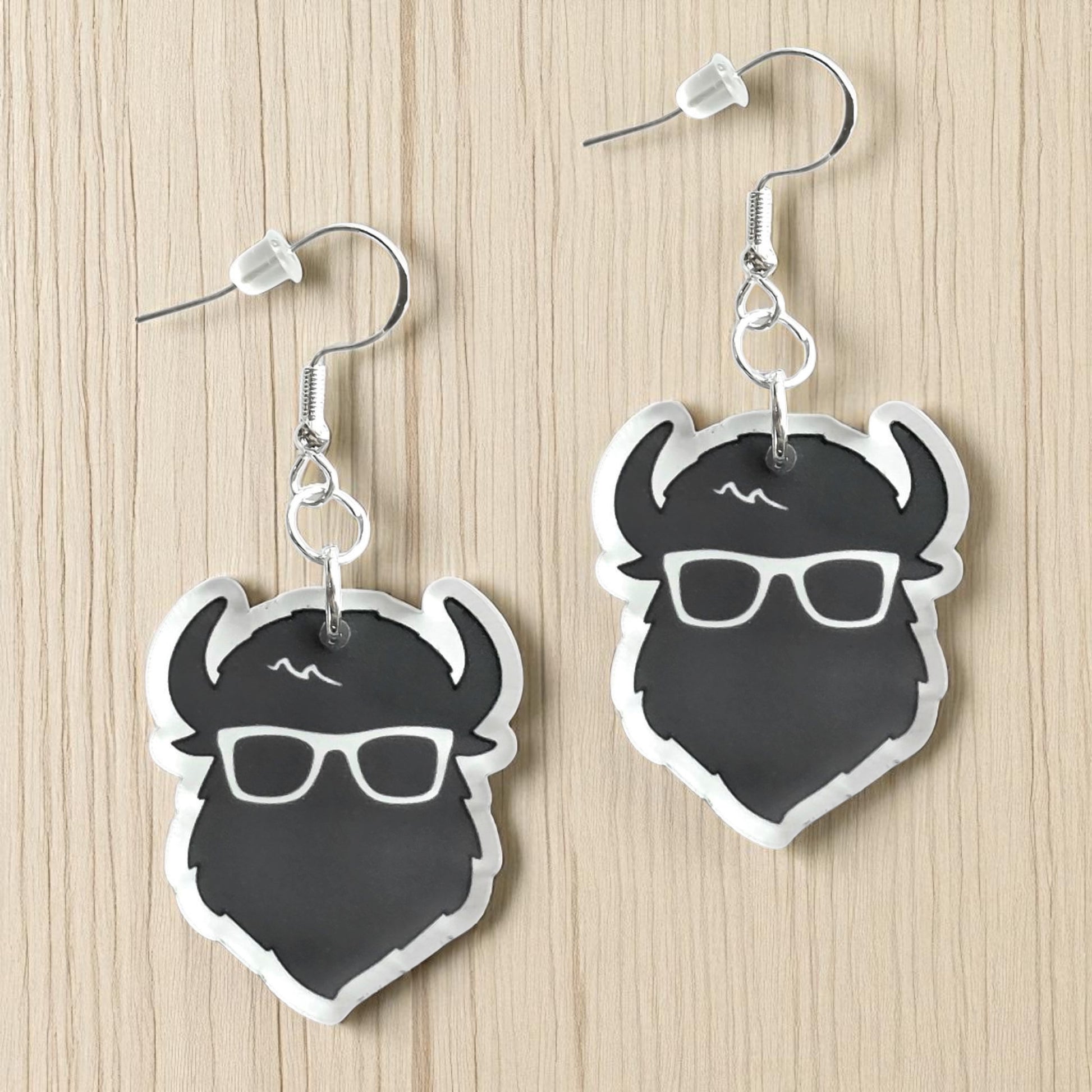 Pair of black and white the curious bison head acrylic earrings displayed on wood surface, graphic bison earrings with sterling silver hooks for travel or souvenir gift