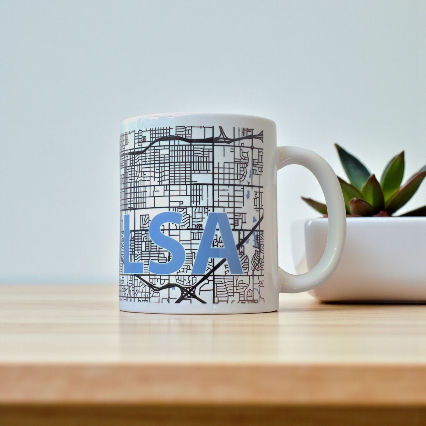 Tulsa city map coffee mug displayed on wood table with plant, 11oz ceramic mug featuring Tulsa street map artwork