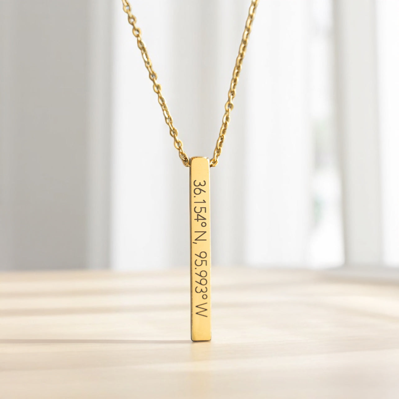 Gold Tulsa coordinates necklace with 36.154°N, 95.993°W engraving, photographed in natural window light on a soft wood surface.