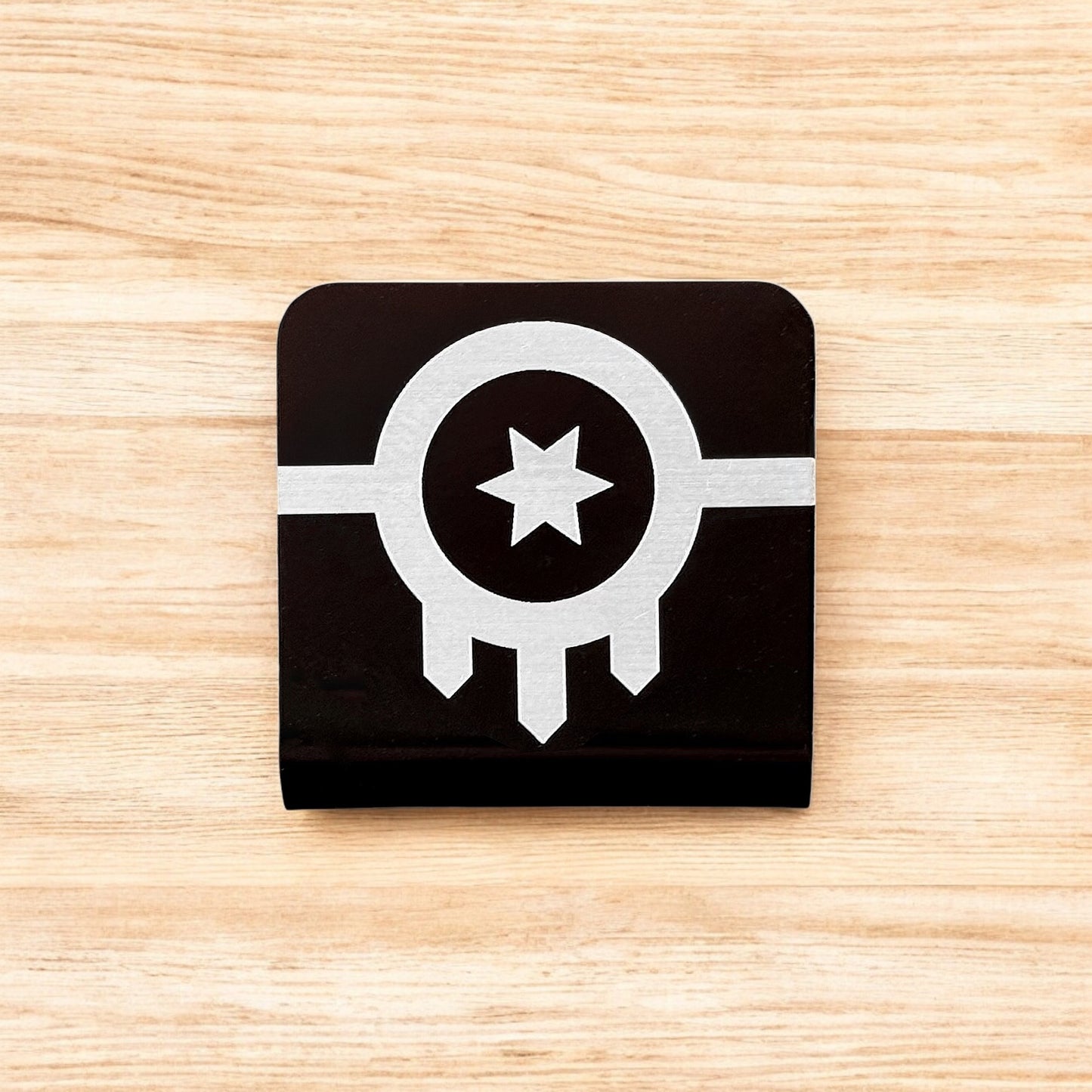 Flat lay of aluminum Tulsa flag hat clip showing square shape, black powder coat, and laser engraved city flag design