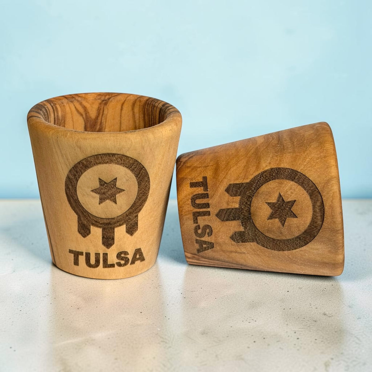 Two Tulsa flag olive wood shot glasses showing natural wood grain variations and laser engraved Tulsa designs, wooden Oklahoma travel souvenirs and Route 66 keepsakes