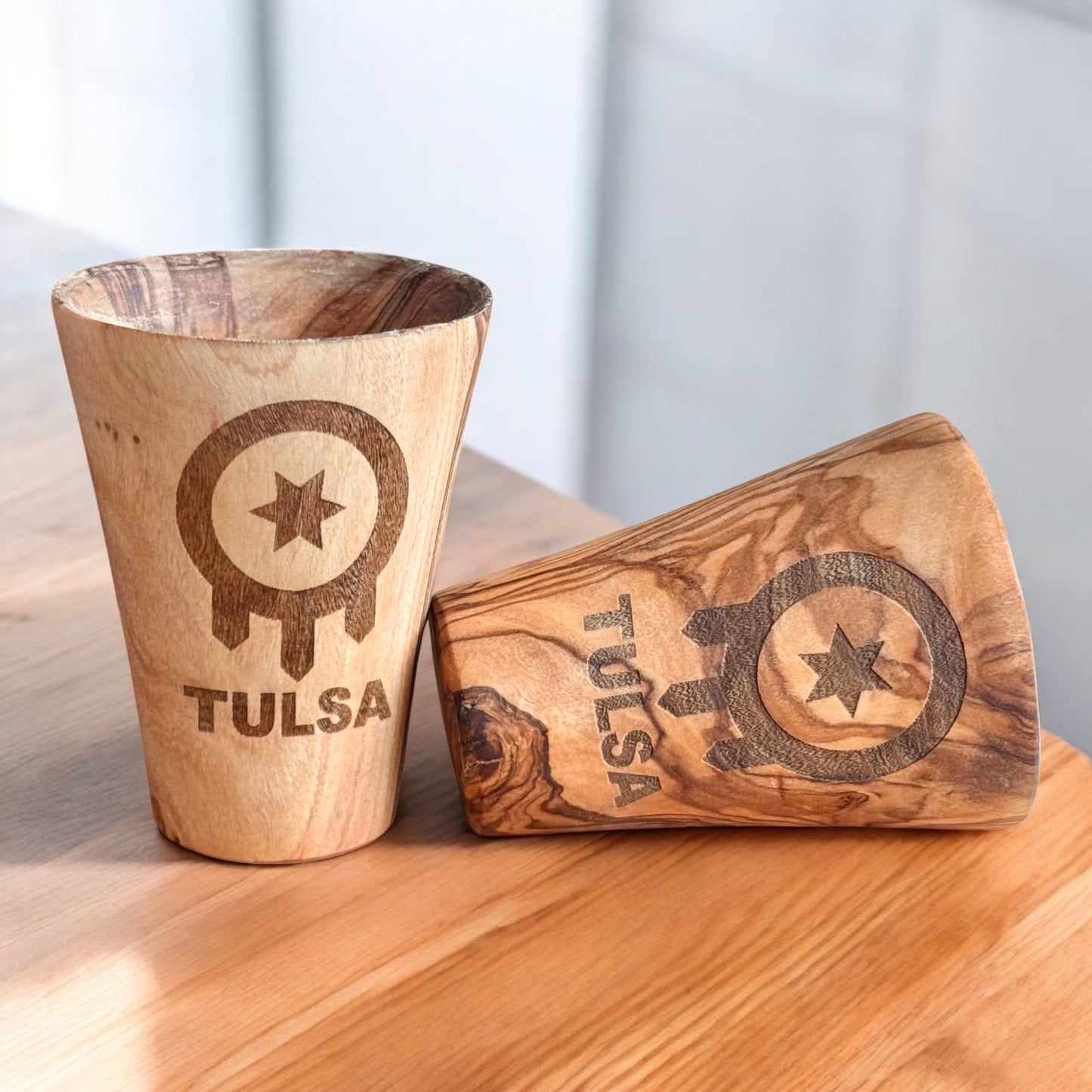 Two olive wood shot glasses engraved with Tulsa flag symbol and TULSA text, natural wood grain Tulsa souvenir drinkware