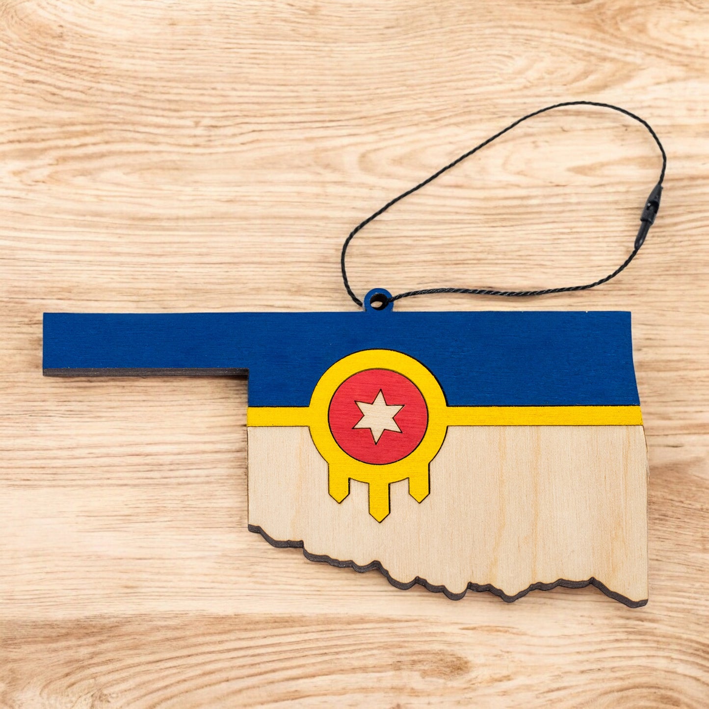 Flat lay of Tulsa flag Oklahoma state ornament with hanging cord on a wood surface