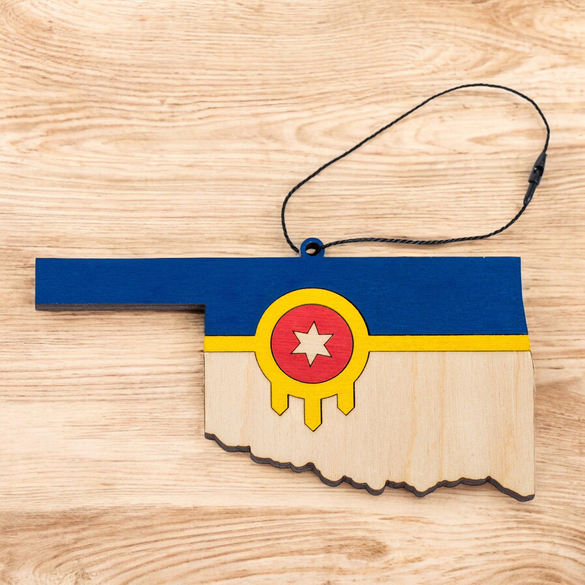 Flat lay of Tulsa flag Oklahoma state ornament with hanging cord on a wood surface
