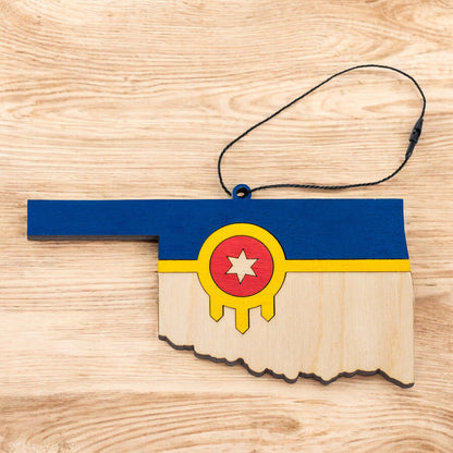 Flat lay of Tulsa flag Oklahoma state ornament with hanging cord on a wood surface